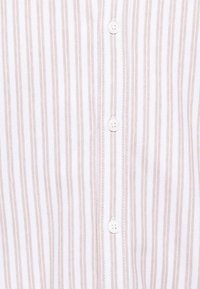 Tissu blanc avec de fines rayures verticales beiges et une rangée centrale de boutons blancs à quatre trous.