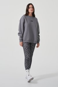 Grauer Sweatshirt mit kleinem schwarzem Logo, kombiniert mit Leggings im Leopardenprint in Grautönen. Das Model trägt weiße Sneaker und Kniesocken.