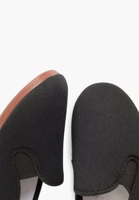 Zwarte instappers met een textiel bovenwerk en een ronde neus. Bruine rubberen zolen met een lichte kromming bij de hak.