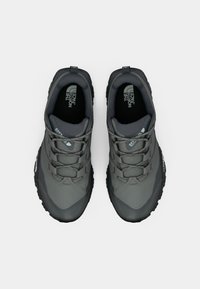 Zapatillas deportivas grises con una parte superior sintética texturizada, múltiples correas de sujeción y una suela de goma con surcos profundos para tracción.