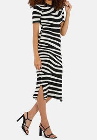 Robe midi rayée noire et blanche avec des manches courtes, texture côtelée, fentes latérales, associée à des sandales à talons hauts noires à lanières.