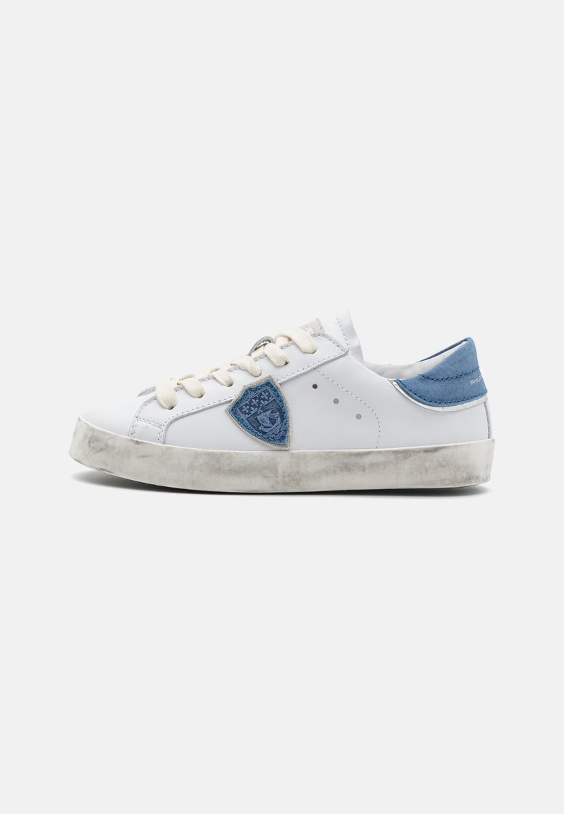 Weiße Ledersneaker mit einem blauen Wildlederakzent, abgerundeter Zehenpartie, beigen Schnürsenkeln und einer leicht abgenutzten grauen Gummisohle. Mit einem Patch-Detail.