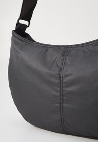 Čierna látková ramenná taška s prešívanou textúrou, s zakriveným tvarom a pevným uchom. Viditeľný jemný mriežkový vzor.