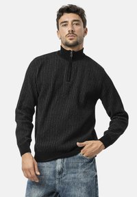 Zwarte zip-neksweater met een verticale ribstructuur. Gemaakt van een zachte, gebreide stof. Heeft een hoge kraag en een contrasterend ritsdetail.