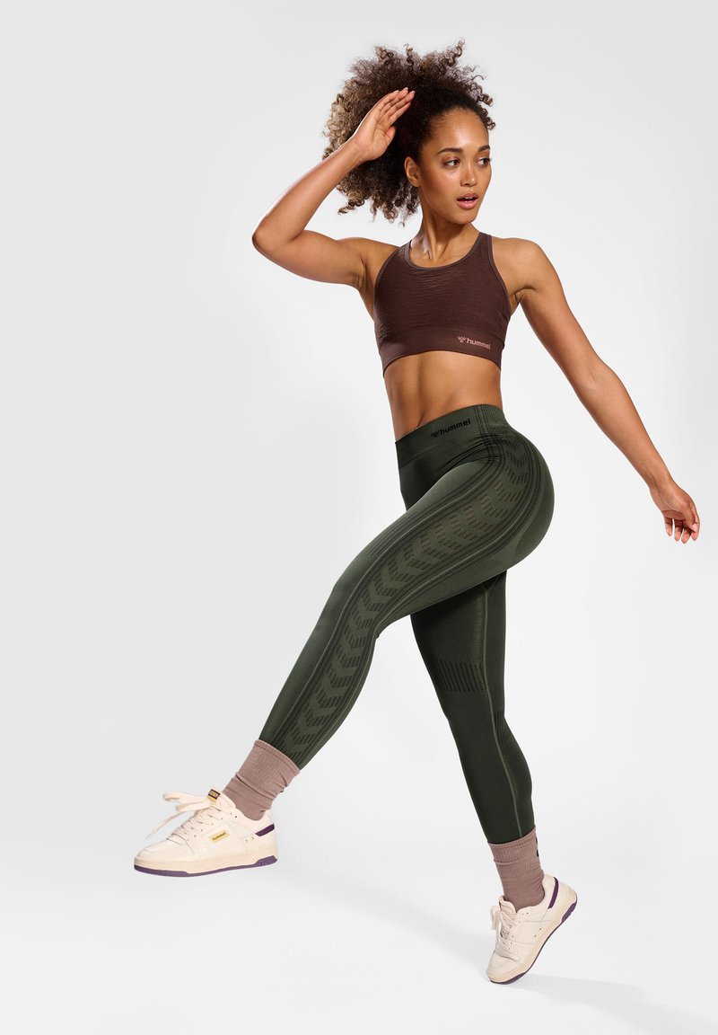 Conjunto deportivo que incluye un sujetador deportivo marrón y leggings verdes con estampado, complementado con zapatillas blancas con acentos morados.