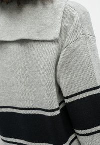 Nahaufnahme eines grauen Strickpullovers mit schwarzen und grauen horizontalen Streifen am Ärmel und Kragen.