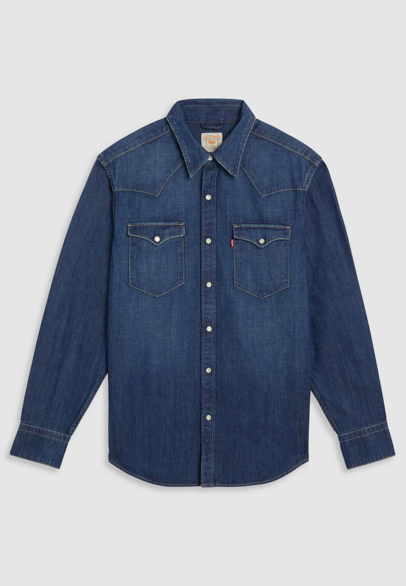 Camisa de denim azul oscuro con mangas largas, cuello puntiagudo, dos bolsillos en el pecho, botones a presión plateados y detalles de costura en contraste.