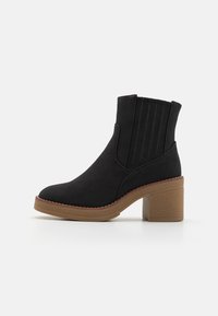 Bottines noires en matériau doux, avec des panneaux latéraux élastiques, un bout rond et un talon bloc texturé marron.