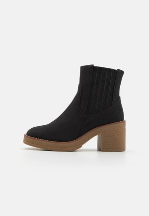 Bottines noires en matériau doux, avec des panneaux latéraux élastiques, un bout rond et un talon bloc texturé marron.
