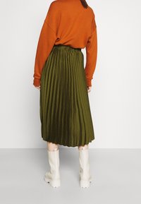 Falda plisada verde con cintura elástica combinada con un sudadera naranja de gran tamaño y botas blancas hasta la rodilla.