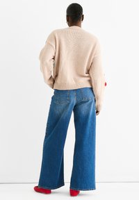 Light beige knitted sweater with a relaxed fit, paired with wide-leg blue jeans. Red shoes complete the outfit. Simple design with minimal detailing.