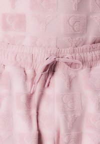 Pink terry cloth joggers featuring a textured pattern of overlapping squares with stylized letters. Drawstring waistband for adjustable fit.