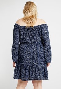 Marinblå off-shoulder klänning med ormtryck, rynkad livstycke och volangkant. Tillverkad av lätt tyg med en texturerad yta.