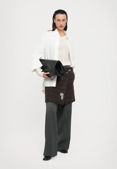 Plică din piele neagră, cămașă albă oversized, top bej, fustă înfășurată cu dungi maronii, pantaloni largi gri și pantofi negri.