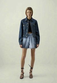 Jeansjacka, mörkblå, knäppning med knappar, två framfickor. Svart crop top, ljusblå slitna shorts, svarta klackar med remmar.