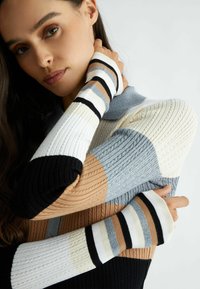 Maglione lavorato a maglia con texture a coste, caratterizzato da blocchi di colore in beige, grigio, nero e bianco, con dettagli a righe sulle maniche.