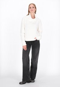 Wit, gezellig oversized trui met een col, gecombineerd met donkergrijze wijde jeans en zwarte enkellaarsjes. Soepele texturen aanwezig.