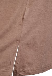 Camiseta de algodón marrón con una abertura lateral, textura suave y dobladillos cosidos. La tela parece ligera y casual.