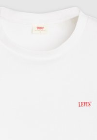 Balts kokvilnas T-krekls ar ribotu struktūru un apaļu kakla izgriezumu. Kreisajā pusē pie apakšmala neliels sarkans "LEVI'S" logotips.