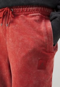 Rote Jogginghosen aus Baumwollmischung mit strukturierter Oberfläche, ausgestattet mit einem elastischen Bund, verstellbarem Kordelzug und einem Logoaufnäher am linken Oberschenkel.