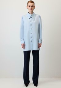 Gaiši zils pogājams krekls ar platu apkakli, sudraba pogām un garām piedurknēm, kombinēts ar tumši ziliem plaša modeļa biksēm un melniem smailiem papēžiem.