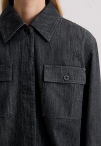 Czarna koszula z denimu z kołnierzykiem na guziki, dwoma kieszeniami na piersiach i teksturowanym wykończeniem. Charakteryzuje się czarnymi guzikami i lekko luźnym krojem.