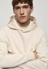Crème-kleurige hoodie met een ontspannen pasvorm, voorzien van een trekkoord in de capuchon en ribgebreide manchetten. Gladde textuur en minimalistisch ontwerp.
