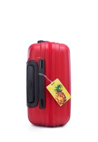 Red hardshell suitcase with textured finish, black handle, and a pineapple-shaped ID tag attached. Compact, rectangular shape with zipper closure.