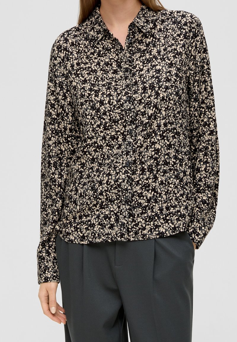 Blusa nera a fiori con bottoni e maniche lunghe, caratterizzata da un denso motivo floreale crema e giallo pallido. Tessuto leggero, vestibilità comoda.