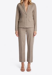 Completo in fantasia houndstooth marrone con giacca su misura dotata di revers a punta, bottone singolo e pantaloni dritti.
