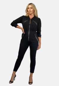 Czarny kombinezon z długimi r ękawami, zasuwany z przodu i z bocznymi kieszeniami. Posiada dopasowany w pasie krój i zwężane nogawki. Teksturowana tkanina z metalowymi akcentami.
