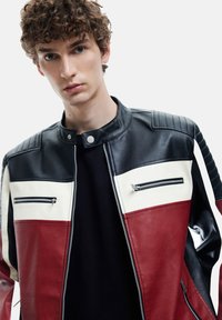 Lederjacke mit schwarzen, roten und weißen Paneelen, Reißverschlusstaschen und Stehkragen. Strukturierte Schulterakzente sorgen für zusätzliche Details.