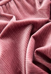 Tissu en velours écrasé de couleur rose poudré, présentant une fine texture côtelée et un éclat subtil, avec des plis doux et fluides.