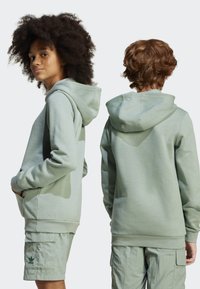 Hoodie verde menta feito de tecido suave, com bolso canguru e capuz. Usado com calções cargo verde claro a condizer.