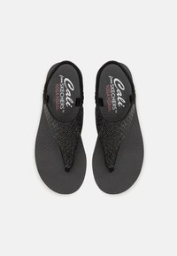 Svart flip-flops med en teksturert, glitrende rem, gummisåle og polstret såle med merkevaren på innersålen.