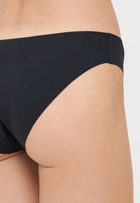 Schwarze Bikiniunterteile mit einem Low-Rise-Schnitt und glatter Textur, die ein schlichtes Design und minimale Hardware aufweisen.