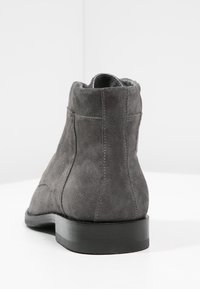 Dark gray suede ankle boot with black sole shown from the back on a white surface against a light gray background.