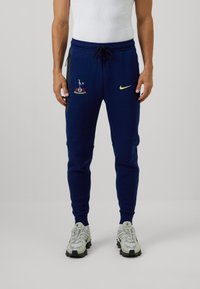 Marineblå sweatpants med elastisk talje, snøre, sidelommer, broderet logo og en kontrasterende gul Nike swoosh.