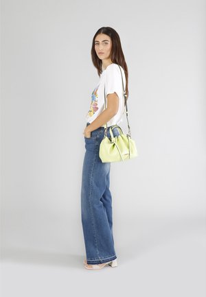 Borsa in pelle verde con doppio manico e tracolla regolabile, abbinata a una t-shirt bianca con grafica e jeans a gamba larga.