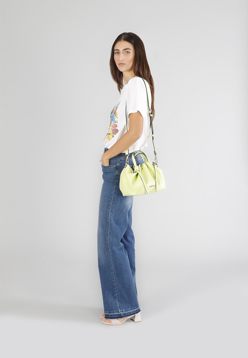 Vihreä nahkakäsilaukku, jossa on kaksinkertaiset kahvat ja säädettävä hihna, yhdistetty valkoiseen graafiseen t-paitaan ja leveälahkeisiin farkkuihin.