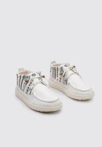 Botas de tobillo de lona blanca con un cuello de tela estampada, cuentas decorativas y costuras en contraste. Suela de goma plana para mayor comodidad.