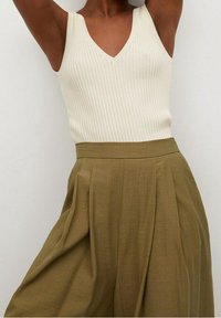 Prążkowany kremowy top na ramiączkach z dekoltem w kształcie litery V, zestawiony z szerokimi oliwkowymi spodniami z zakładkami i teksturowanym wykończeniem.