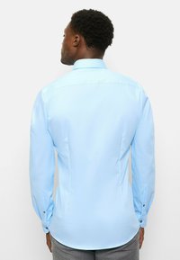 Hellblaues langärmeliges Hemd mit spitzem Kragen, figurbetontem Design und Knopfverzierungen an den Manschetten. Glatte Textur mit einfarbiger Optik.