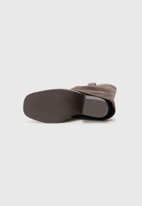 Bota de tornozelo em pele castanha com ponta arredondada, salto baixo e sola texturizada. A bota apresenta um design de dobra sem adornos.