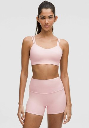 Light pink sports bra with slim straps and matching high-waisted shorts, made from smooth stretch fabric, designed for comfort.