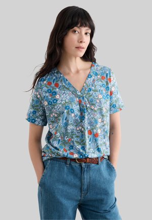 Blouse à motifs floraux en bleu clair, avec des manches courtes, un col en V et une coupe ample. Associée à un jean en denim taille haute.