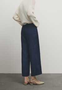 Marineblauwe wijde broeken van denim, met een hoge taille, strakke lijnen en een subtiele textuur. Gekleed met een lichtgebreid crèmekleurig sweater en beige schoenen.