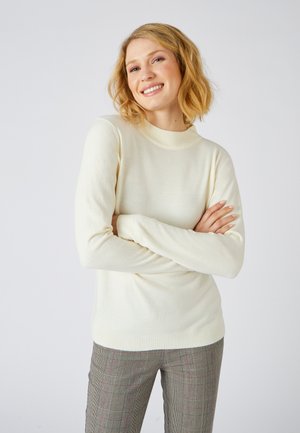 Jersey crema con cuello redondo acanalado y mangas largas, hecho de una tela suave. Combinado con pantalones de cuadros estampados.