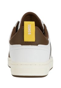 Vit och brun sneaker med en texturerad yta, med en gul logotag vid hälen, stickade detaljer och en gummisula.