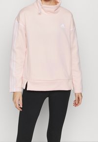 Sweat à capuche rose avec un col montant, en tissu doux et texturé, présentant des rayures blanches sur les manches et un logo Adidas.